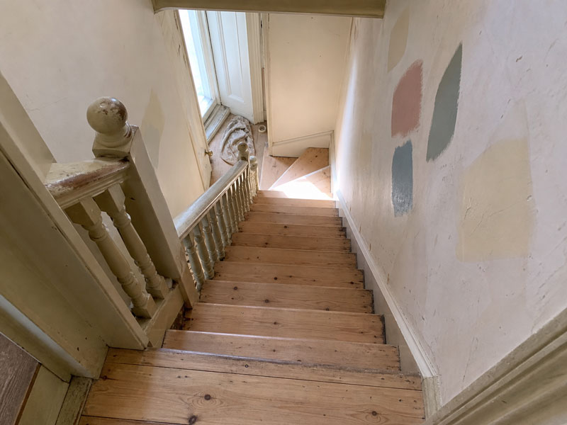 Worn staircase and landing before sanding, dull boards and paint test patches on the wall above