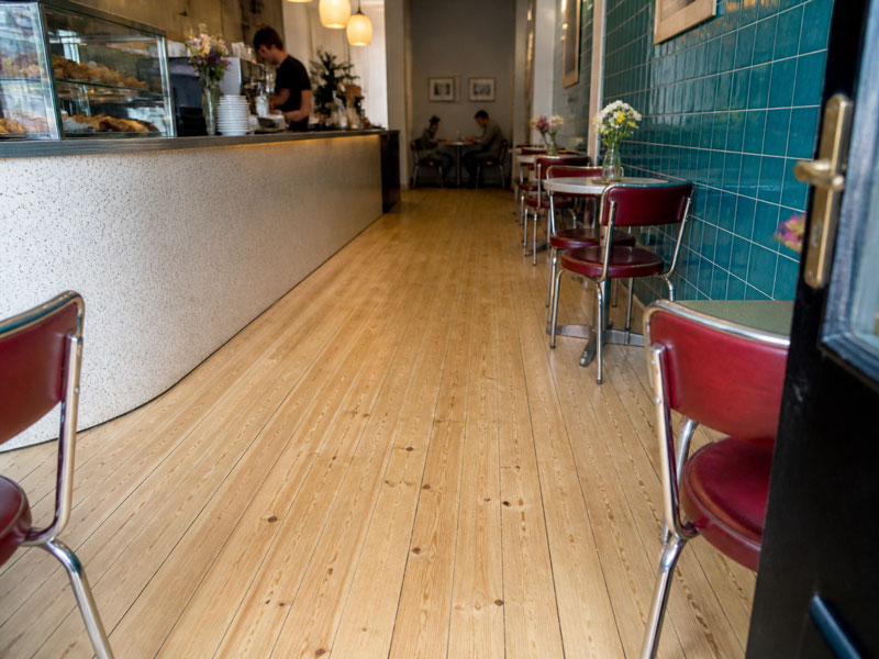 Finished café floor in daytime use, staff serving behind the counter and customers seated at tables on the newly sanded boards