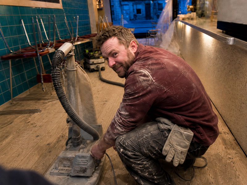 Ian sanding the café floor overnight with an edging sander, chairs stacked on the counter and the shop closed for the job