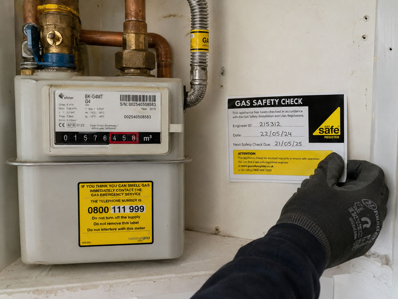 Gloved hand applying a Gas Safe safety check label to a domestic gas meter after inspection
