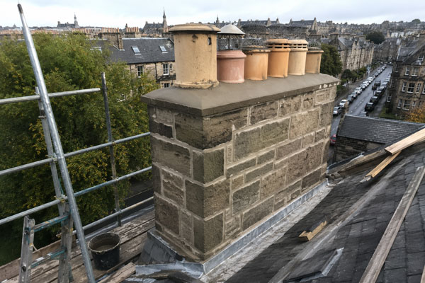 Rebuilt sandstone chimney stack with new chimney pots fitted, scaffold alongside, Edinburgh rooftops behind