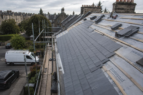 Elevated view of a full slate re-roof mid-progress on an Edinburgh tenement, scaffold up, works van parked on the street below