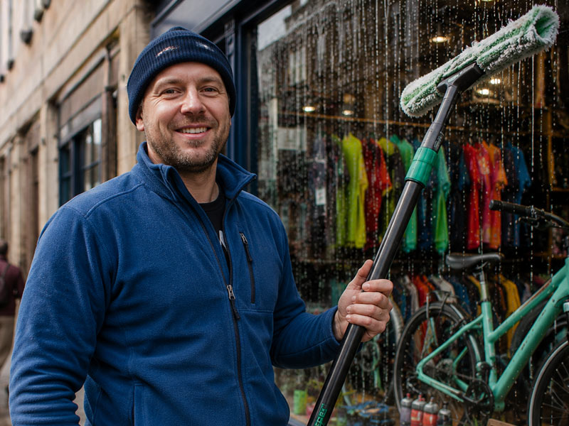 John Dean, Edinburgh window cleaner, smiling outside a shopfront with his water-fed pole
